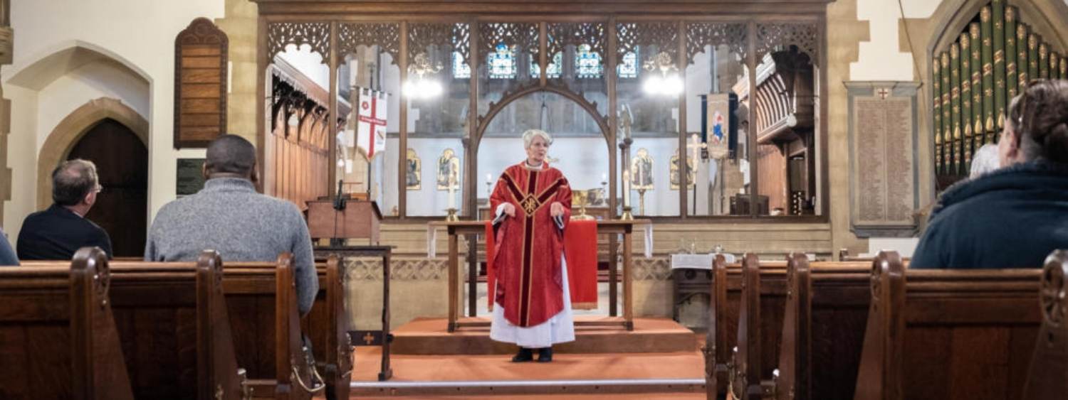 Female clergy in red robes standing at the altar talking to the congregation seated in pews