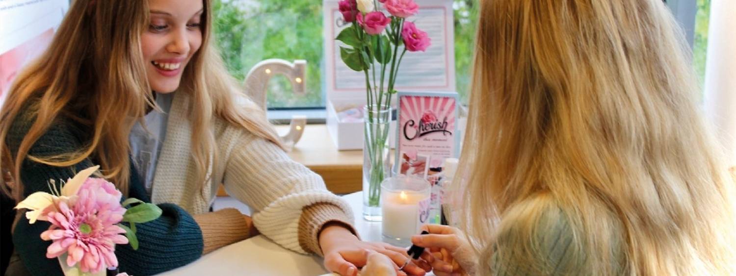 Two young teenagers sitting smiling at a manicure table painting each others nails